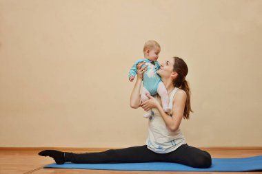 Genç anne bebeğiyle birlikte fiziksel yoga egzersizleri yapıyor.