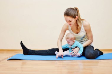 Genç anne bebeğiyle birlikte fiziksel yoga egzersizleri yapıyor.