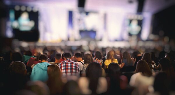 Многие молодые люди в большом зале слушают оратора
