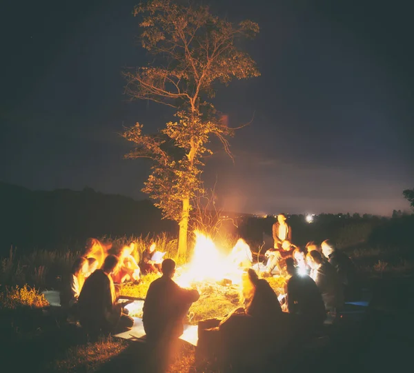 Společnost mladých lidí sedí kolem ohně a s — Stock fotografie