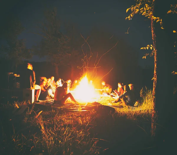 Die Gesellschaft junger Leute sitzt am Lagerfeuer und — Stockfoto