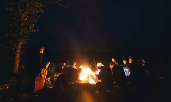 A companhia de jovens estão sentados em torno da fogueira e s — Fotografia de Stock