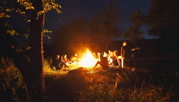 La compagnie des jeunes sont assis autour du feu de joie et s — Photo