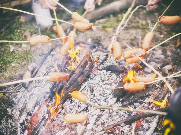 Uma grande empresa de pessoas está fritando salsichas em varas de madeira ov — Fotografia de Stock
