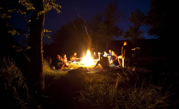 The company of young people are sitting around the bonfire and s Royalty Free Stock Photos