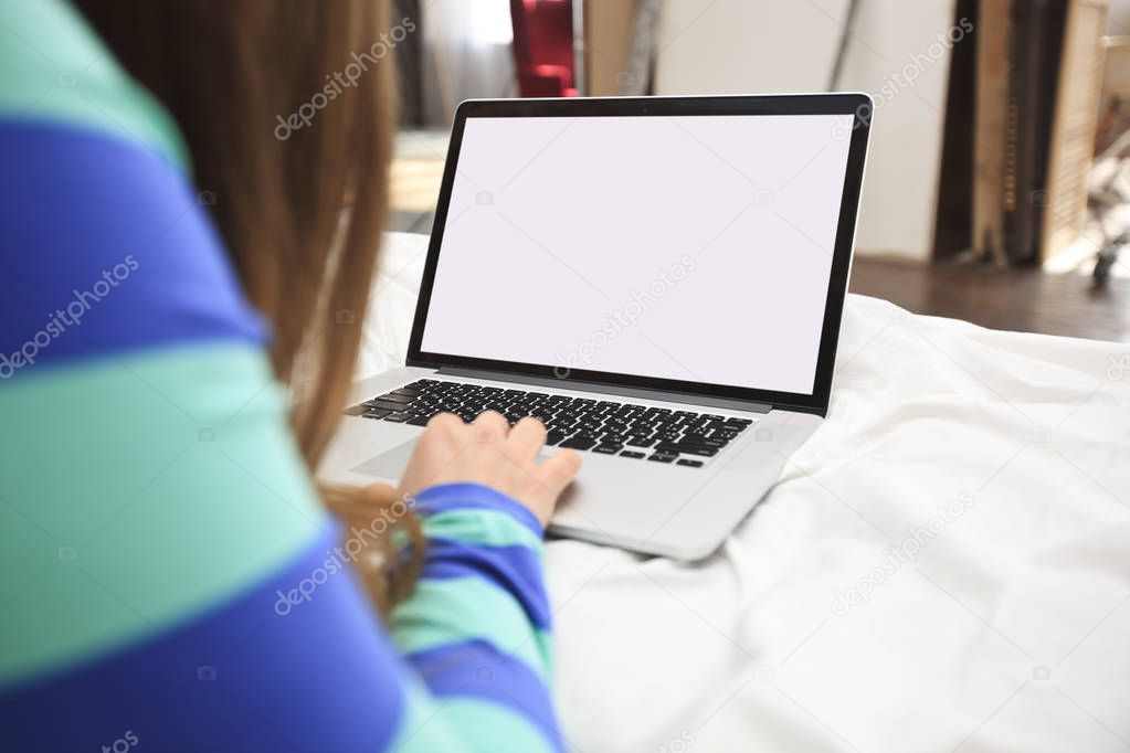 The young woman is lying on the bed with a laptop 