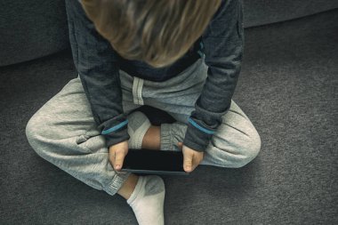 Küçük çocuk kanepede tek başına oturuyor ve ona bakıyor.