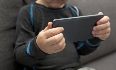 Küçük çocuk kanepede tek başına oturuyor ve ona bakıyor.