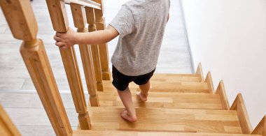 Çocuk evdeki ahşap merdivenlerden aşağı iniyor.