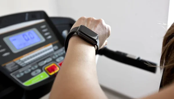 The woman is running on treadmill at home and looking on her sma — Stock Photo, Image