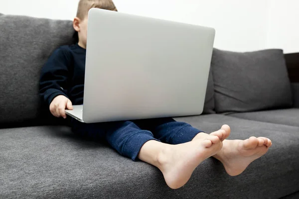 Çocuk kanepede oturmuş dizüstü bilgisayarını tutuyor ve izliyor. — Stok fotoğraf