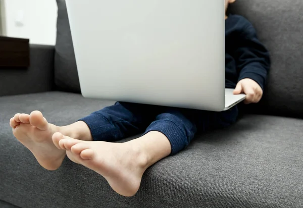 Barnet sitter i soffan och håller i laptopen och tittar — Stockfoto