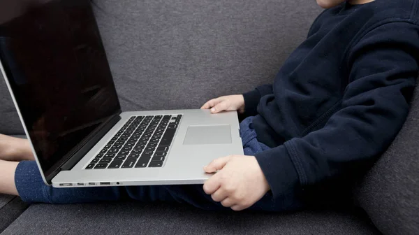 Çocuk kanepede oturmuş dizüstü bilgisayarını tutuyor ve izliyor. — Stok fotoğraf