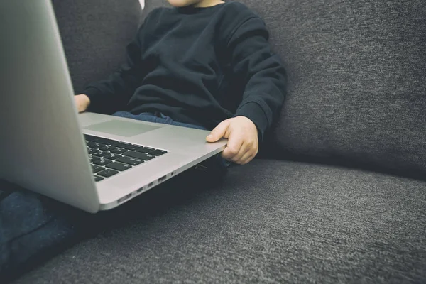 Barnet sitter i soffan och håller i laptopen och tittar — Stockfoto