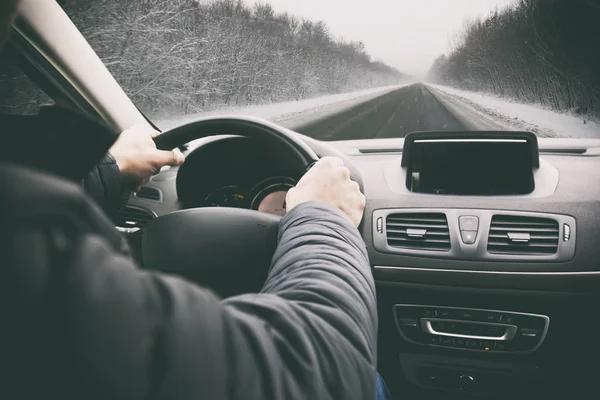 O jovem está dirigindo em seu carro através de uma estrada nevada — Fotografia de Stock