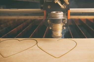 Laser cutting machine is cutting hearts in the wooden plank clipart