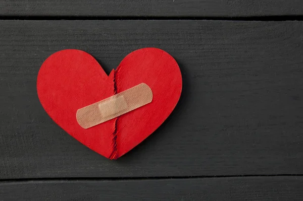 Δύο κομμάτια κόκκινης ραγισμένης ξύλινης καρδιάς κολλημένα με ένα μπάλωμα. Έννοια o — Φωτογραφία Αρχείου