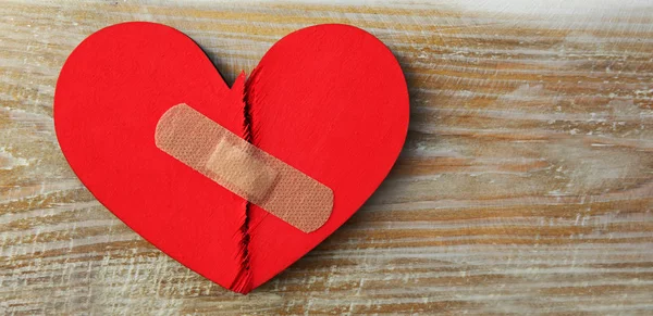 Two parts of red broken wooden heart taped by a patch. Concept o — Stock Photo, Image