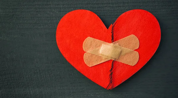 Two parts of red broken wooden heart taped by a patch. Concept o — Stock Photo, Image