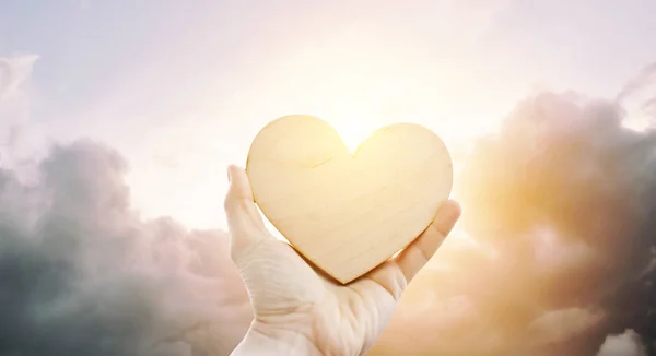 Het houten hart in de hand van de vrouw tegen zonsondergang — Stockfoto