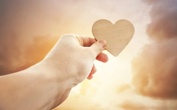 O coração de madeira na mão da mulher agains por do sol — Fotografia de Stock