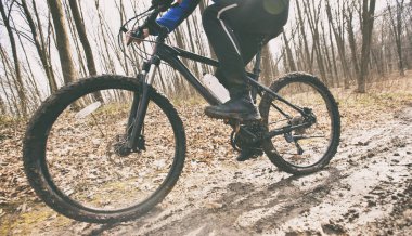 Bisikletçi, baharın başında ormanda toprak yolda dağ bisikletine biniyor. 