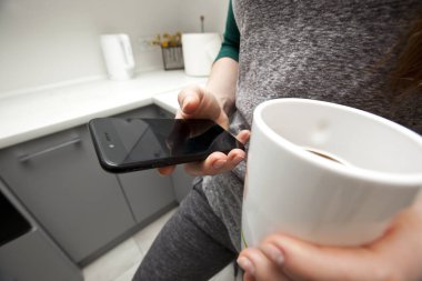 Kadın sabah kahvesini içiyor ve sosyal ağlarını telefonundan kontrol ediyor.