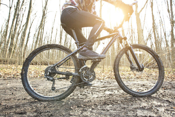 Велосипедист едет на горном велосипеде по грунтовой тропе в лесу ранней весной
 