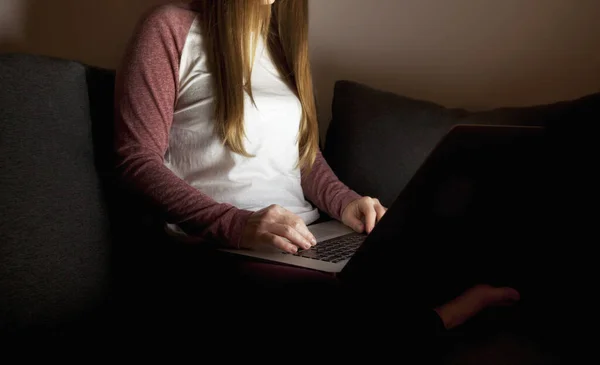 Woman works late sitting on the sofa with laptop