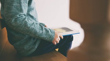 Çocuk evdeki ahşap merdivenlerde oturmuş kağıt kitap okuyor.