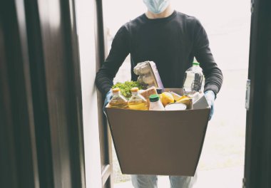 Kurye, plastik eldiven ve tıbbi maske takarak marketten aldığı yiyeceklerle birlikte karton eko kutusunu getiriyor.