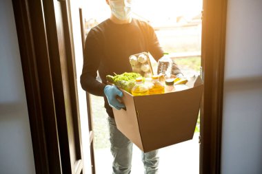 Kurye, plastik eldiven ve tıbbi maske takarak marketten aldığı yiyeceklerle birlikte karton eko kutusunu getiriyor.