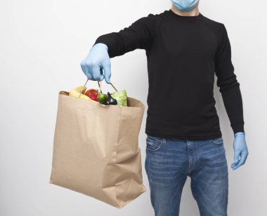 Kurye, bakkaldan aldığı kese kağıdını elinde tutuyor ve lateks eldivenler giyiyor.