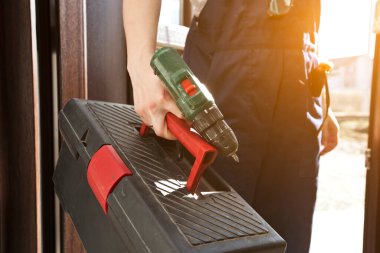 İş üniformalı kadın tamirci elinde alet çantası ve diğer ekipmanlarla eve geliyor.