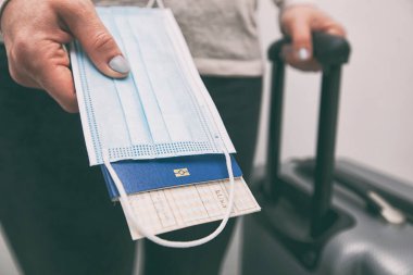 Pasaportu elinde tutan kadın, tren bileti ve sağlık maskesi ile birlikte 19 saat sonrası seyahatinde olmazsa olmaz bir şey.