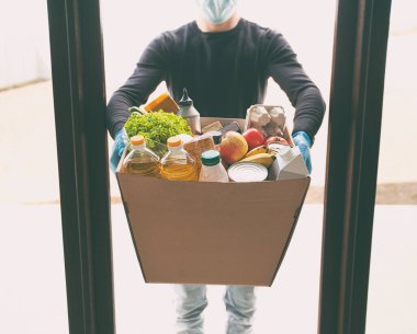Kurye, plastik eldiven ve tıbbi maske takarak marketten aldığı yiyeceklerle birlikte karton eko kutusunu getiriyor.