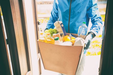 Kurye, plastik eldiven ve tıbbi maske takarak marketten aldığı yiyeceklerle birlikte karton eko kutusunu getiriyor.