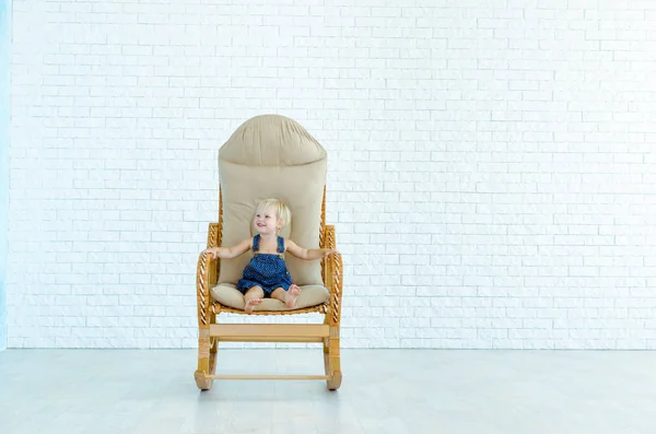Little girl rides a rocking chair on the background of a white brick wall.