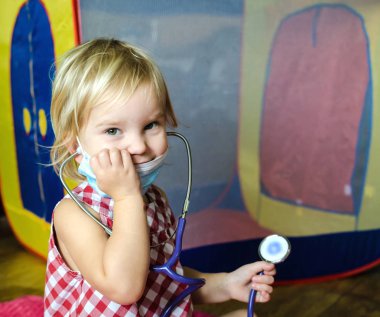 Doktor onun bebek ile oynayan küçük bir kız. Ameliyat maskesi ve elinde bir stetoskop giymiş bir çocuk.
