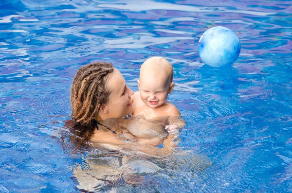 Mom teaches a child to swim. Coach teaches todler to swim in the pool. They play with a ball.