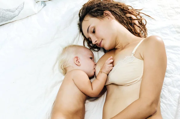 Жінка годує грудьми свою дитину. Мама і дочка лежати на ліжку. — стокове фото