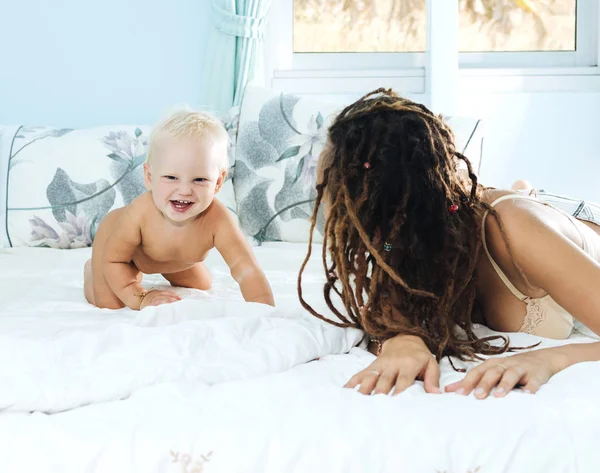 Mãe e filha deitam-se na cama. Mulher e criança em um quarto luminoso. Menina com dreadlocks . — Fotografia de Stock