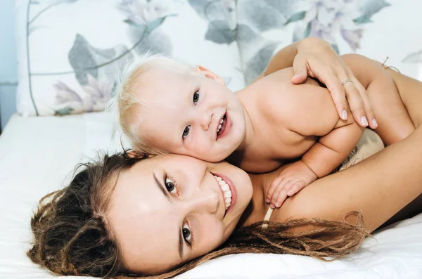 Moeder en dochter liggen op het bed. Vrouw en kind in een lichte kamer. Meisje met dreadlocks. — Stockfoto