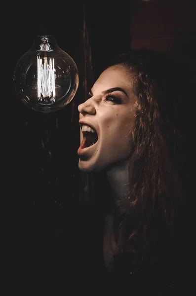 Frau in der Dunkelheit schreit auf der Lampe. Emotionales Foto. — Stockfoto