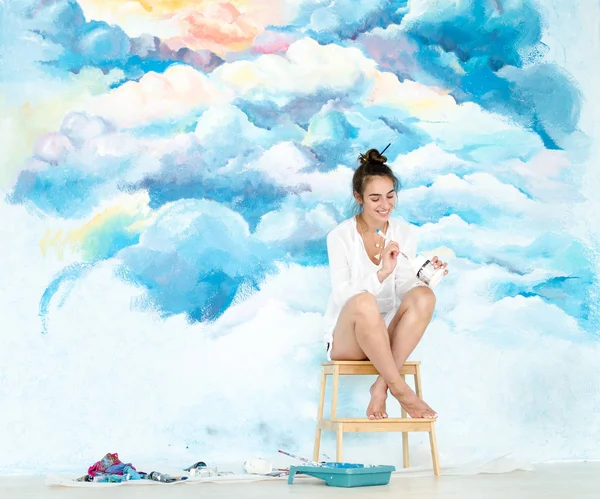 Молодая художница. Она рисует небо на стене . — стоковое фото