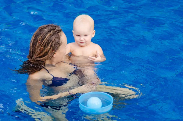 Mutter und ihr Kind im Pool. Frau spielt mit seiner kleinen Tochter mit einem Ball. — Stockfoto