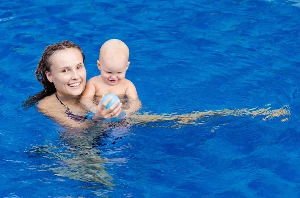 Madre y su hijo en la piscina. Mujer jugando con una pelota con su hijita . — Foto de Stock
