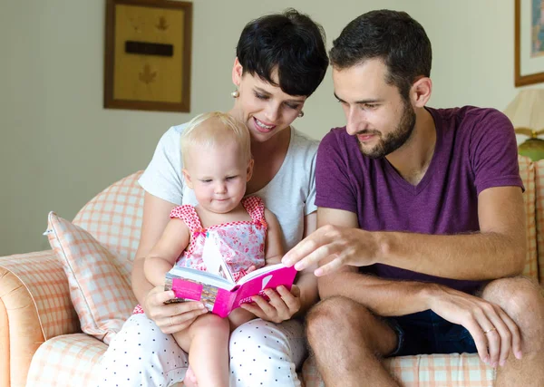 Мати, батько і дочка читають книжку. Сім'я сидить на дивані . — стокове фото