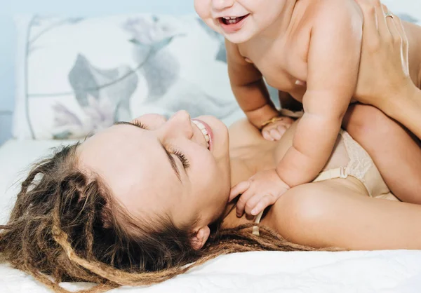 Moeder en baby op het bed. Een vrouw en haar todler spelen liggen in de slaapkamer. — Stockfoto