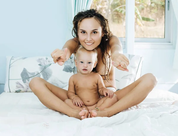 A mãe e o bebé na cama. Uma mulher e seu todler estão brincando deitados no quarto . — Fotografia de Stock